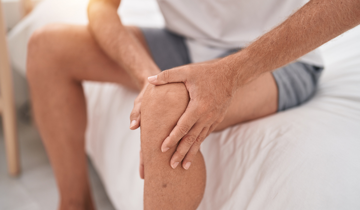 Brightly-Biomarkers-young-blond-man-suffering-knee-injury-sitting-bed-bedroom
